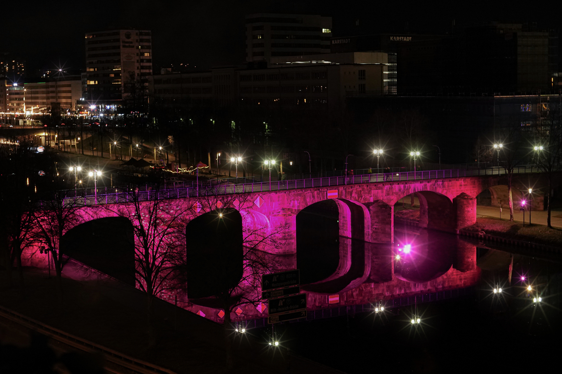 Pink beleuchtete Brücke über die Saar bei Nacht in Saarbrücken mit Spiegelung im Wasser