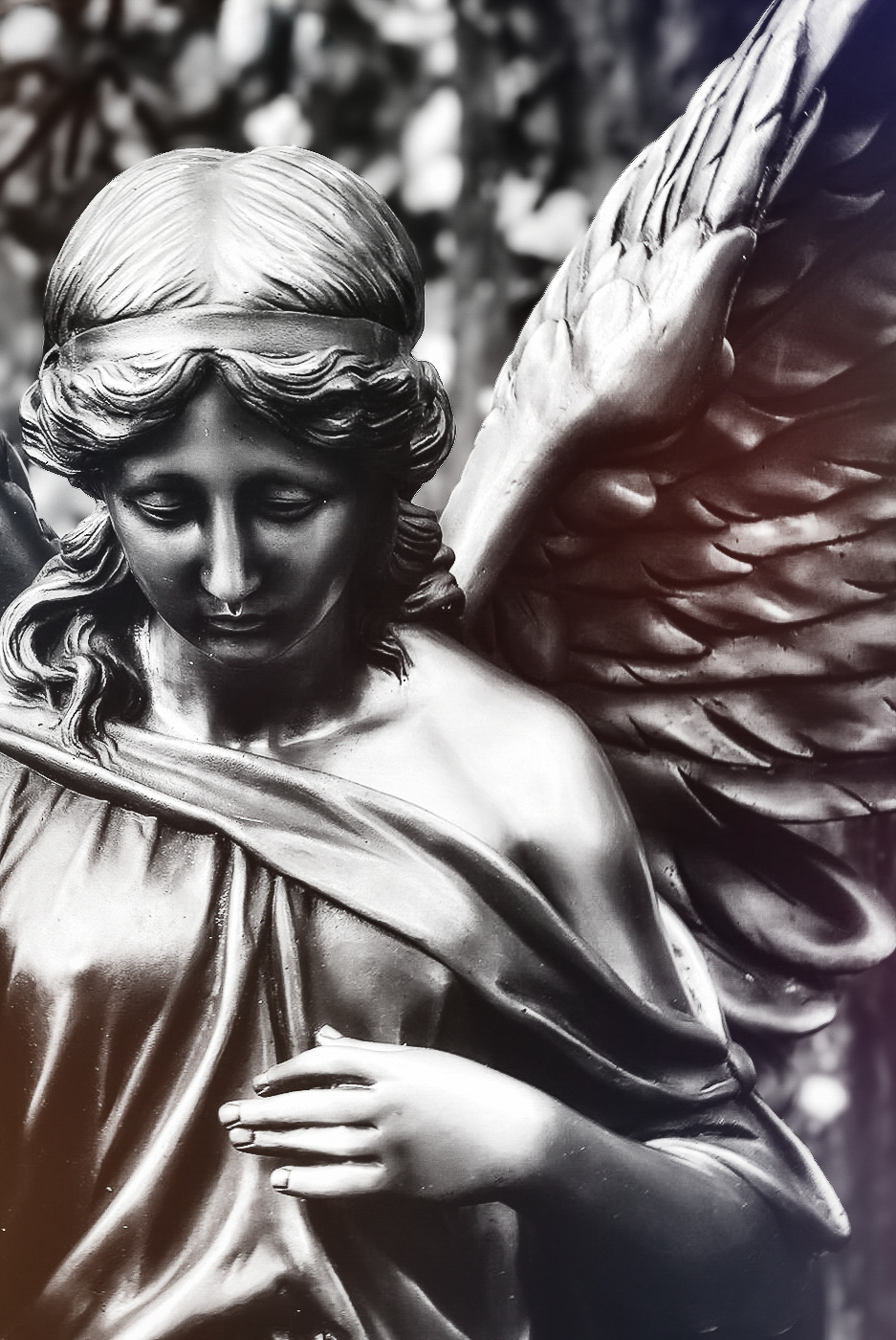 Engelsstatue in Schwarzweiß mit gesenktem Blick, detailreich ausgearbeiteten Flügeln und weich verlaufenden Lichtreflexen, aufgenommen in einem Friedhofsumfeld mit experimentellem, leicht mystischem Lichtspiel