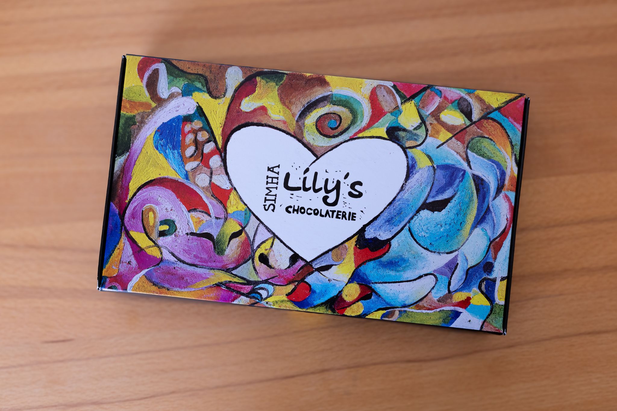 Geschlossene Schokoladenbox von Lilly’s Chocolaterie mit farbig handgemalter Verpackung auf Holzuntergrund