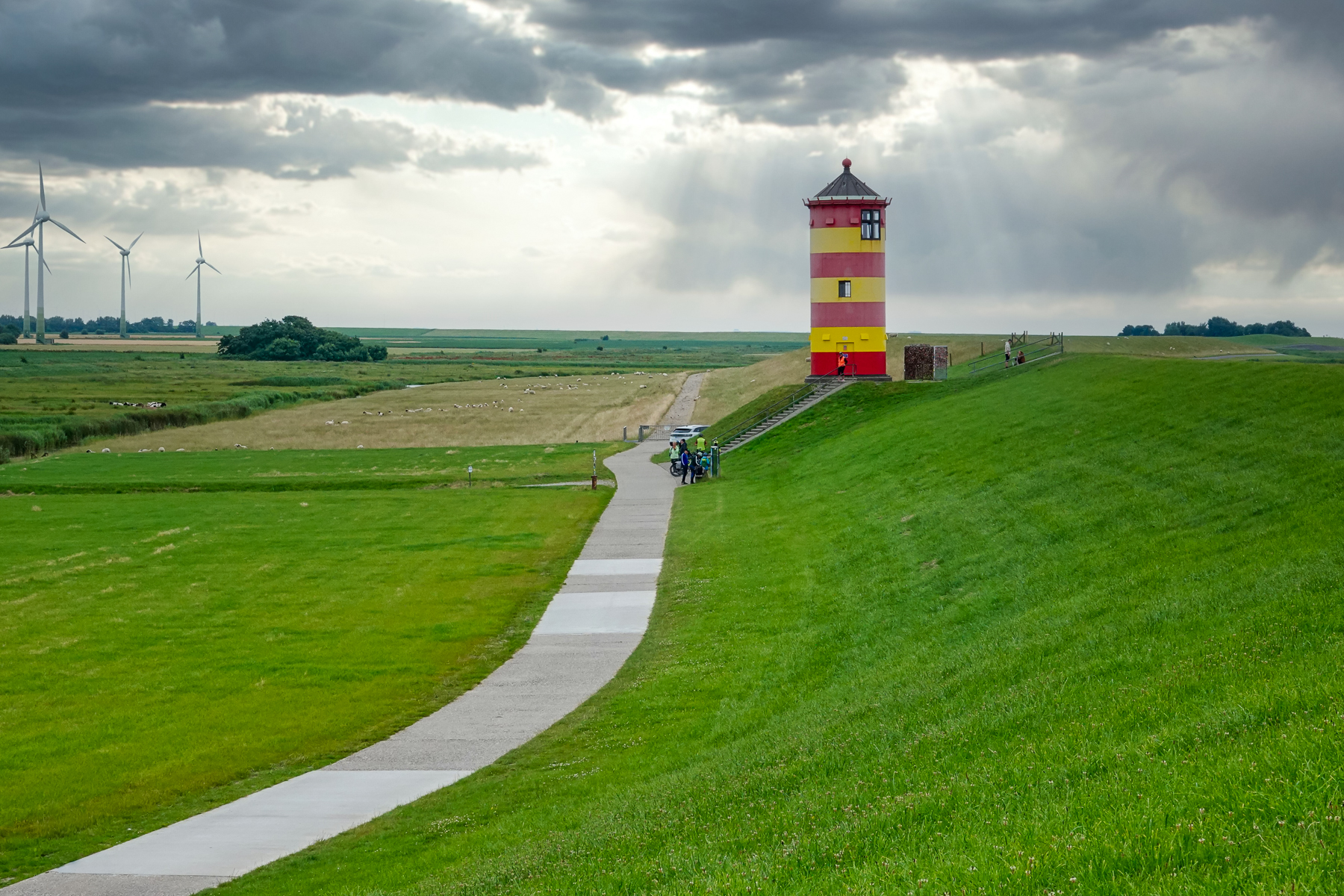 Pilsumer Leuchtturm in Ostfriesland, aufgenommen mit Weitwinkelperspektive, grüner Deich, Weg zum Leuchtturm, dramatische Wolken und Sonnenstrahlen