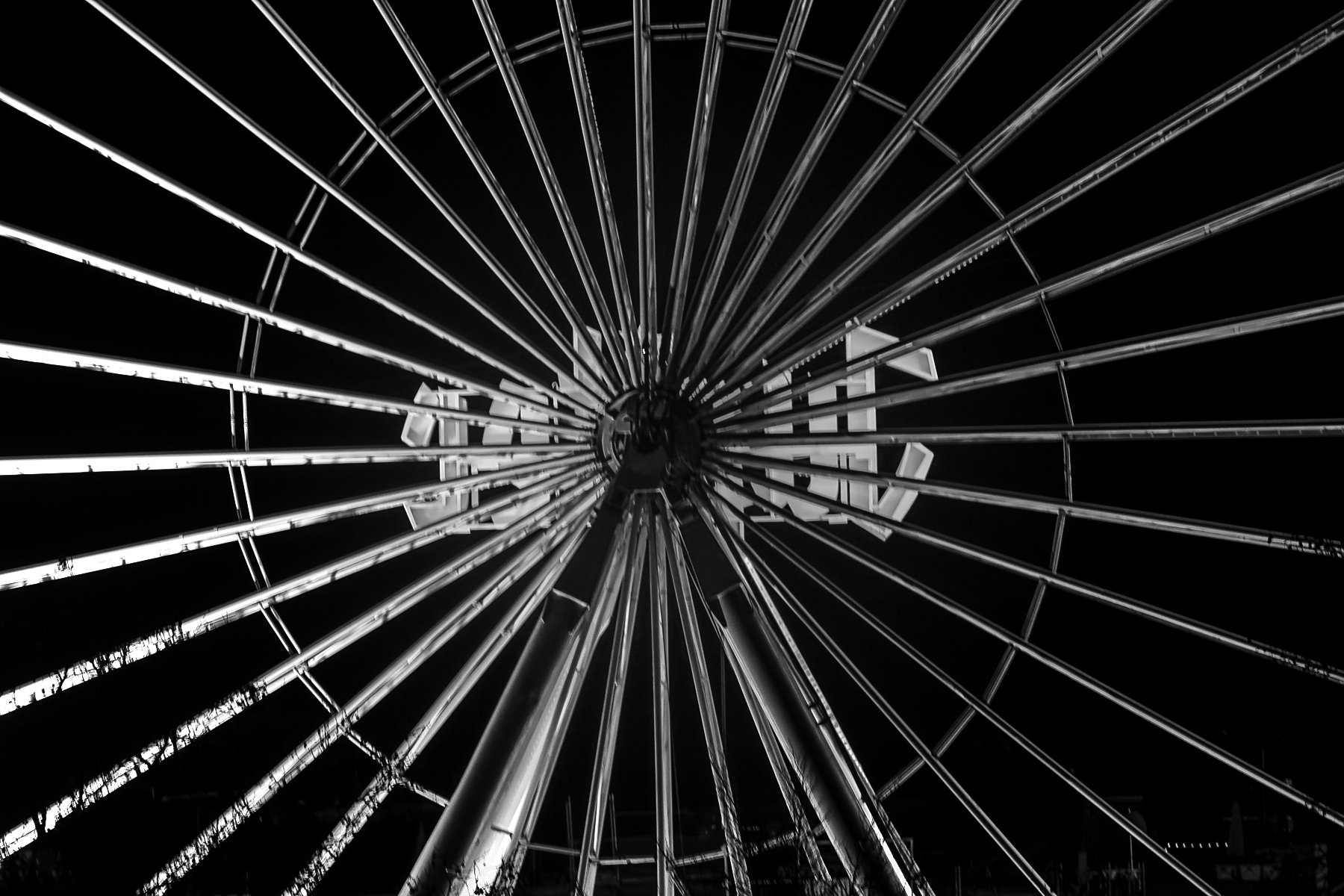Schwarzweißaufnahme eines Riesenrads von unten mit radialen Streben bei Nacht